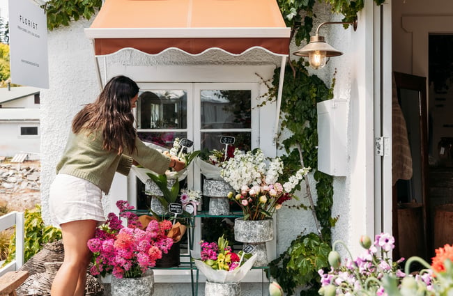 A staff member attends to bouquets in pots on racks under an orange awning outside The Workroom.