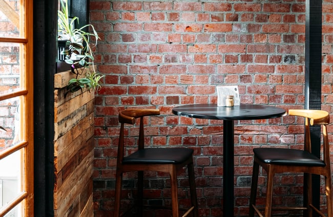 Tall seating and a table next to a brick wall inside Three High Street cafe in Rangitikei.