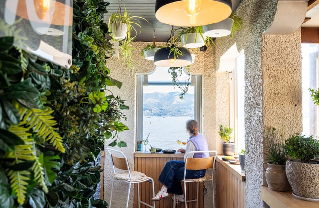 Woman sitting next to window at Tini bar with food and cocktails looking out on to waterfront views