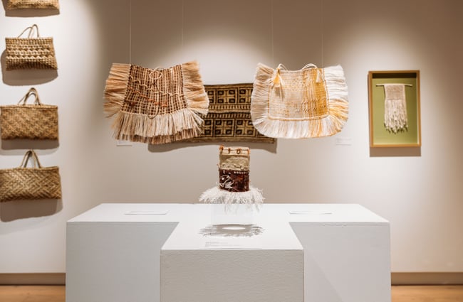 Weaved bags and mats on display inside a gallery.