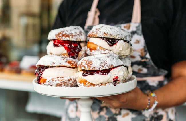 Person holding plate of cream donuts from Tomboy, Wellington.