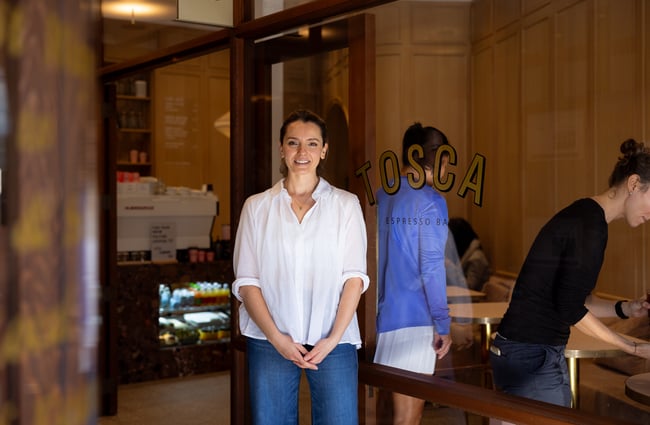 Owner of Tosca Blerta Rakovica standing and smiling by the cafe entrance
