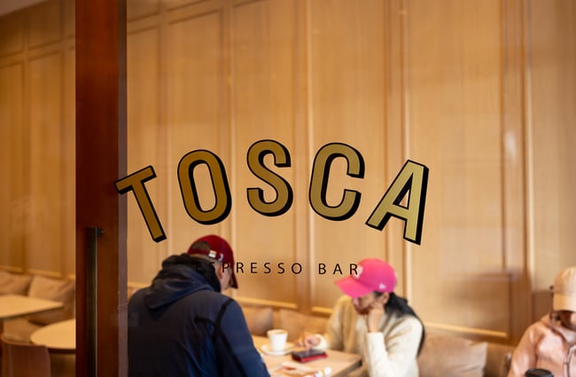 Golden 'Tosca' window decal with customers drinking coffee in background