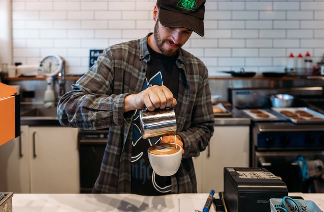 Barista pouring milk into freshly made coffee at cafe