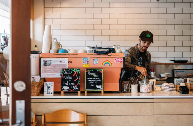 Barista making coffee in contemporary cafe space with signs for chilli hot chocolate and mochas on the counter