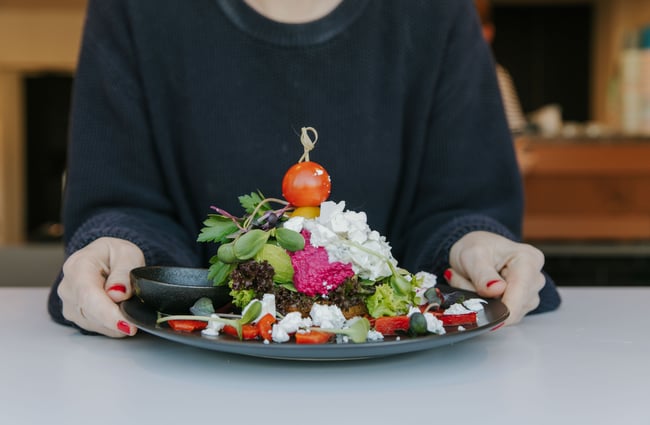 Two hands holding a plate of avocado and beetroot on a toast.