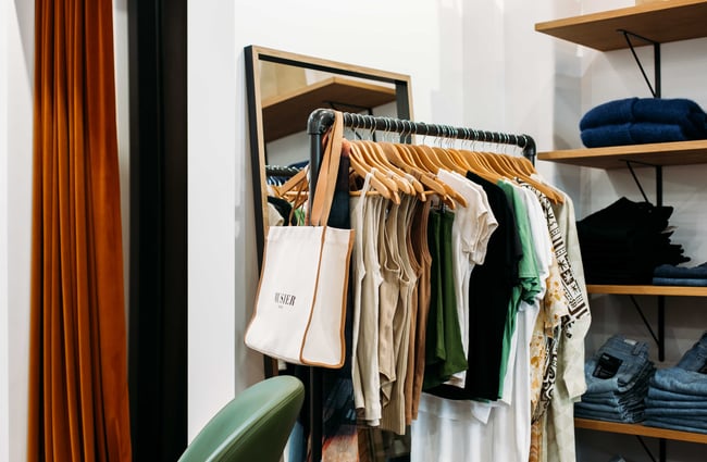 A black industrial clothing rack holding clothing on wooden hangers.