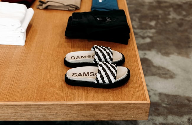 Black and white stripped SAMS sandals sitting on a wood table.