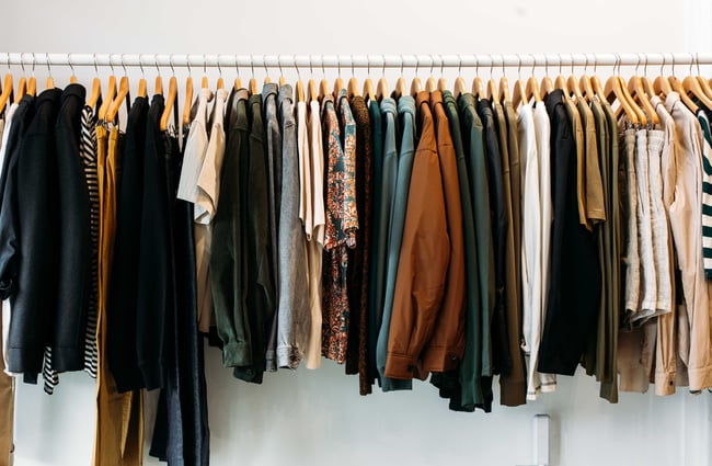 A clothing rack filled with top and pants in different neutral tones.