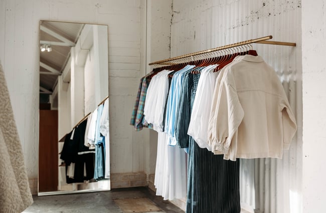 A rack of clothing being reflected in a floor length mirror at twenty-seven names.