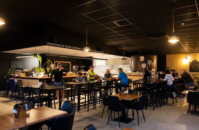 Interior of Two Thumb Harbourside with people drinking at tables and man walking away from bar with a beer