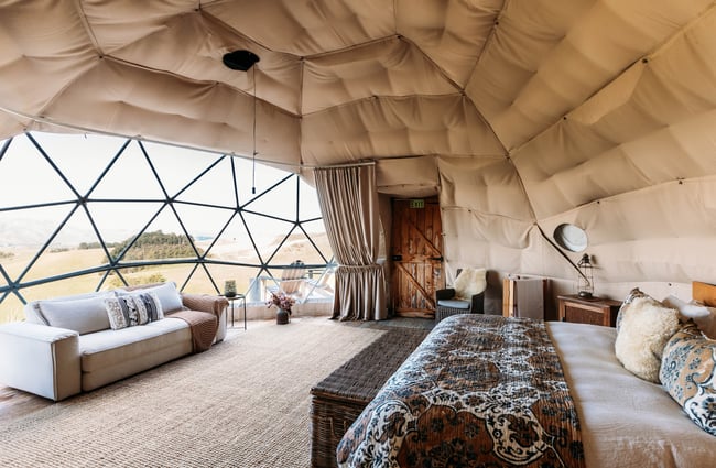 Couch and bed inside a glamping pod looking out across the green landscape in Kurow