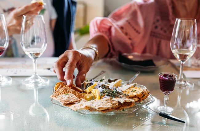 Woman in pink blouse reaching for cheese and crackers next to glasses of wine