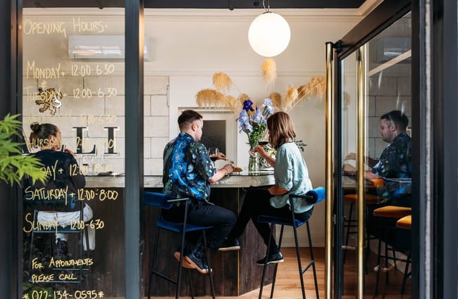 Looking through doorway into VALLI Wine Bar where two guests are sitting together at the bar drinking wine