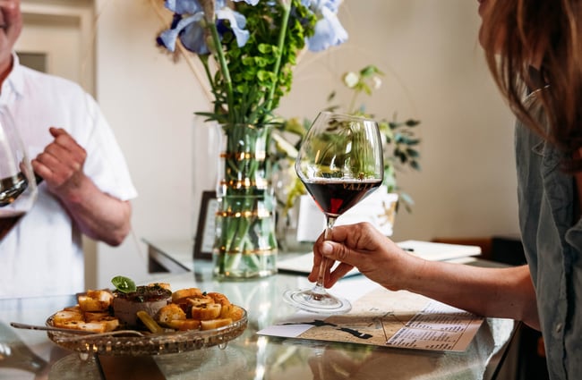 Woman holding glass filled with red wine next to a plate of pate and croutons