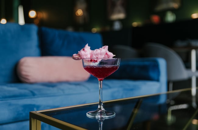A close up of a pink cocktail with pink candy floss.