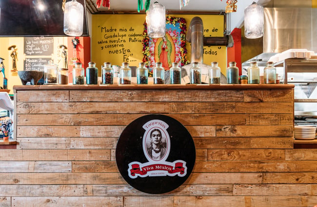 Wooden counter with photo of Frida Kahlo on front and jars of spiced lined up along the shelf