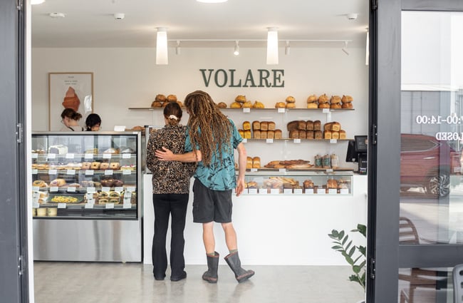 A couple is standing in front of the cabinet looking at the breads and pastries at Volare Bread.