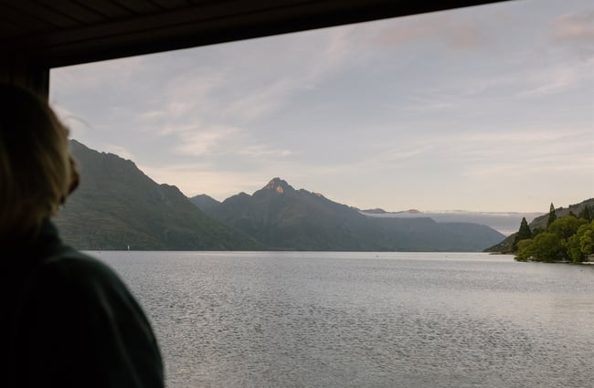 Person standing in sauna looking out at waterfront view