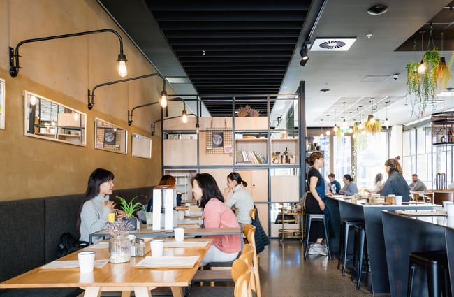 Customers dining at tables inside a light and bright cafe interior.