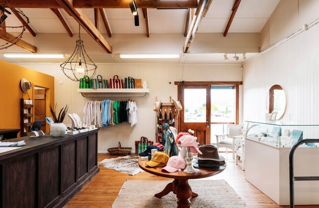Interior of Whistle & Pop store with a dark wooden counter, glass jewellery cabinets and a selection of hats, bags and t-shirts.