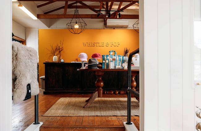 Looking through entranceway into Whistle & Pop's shop with orange feature wall, jute rug and caps and bags on table in the middle of the store
