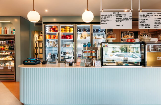 Blue counter at Whitestone Cheese Deli & Diner with fridge full of cheese and menu board hanging over cabinet