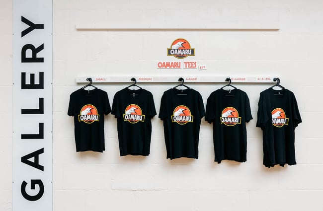 Row of Ōamaru branded t-shirts hanging along wall next to big 'Gallery' sign