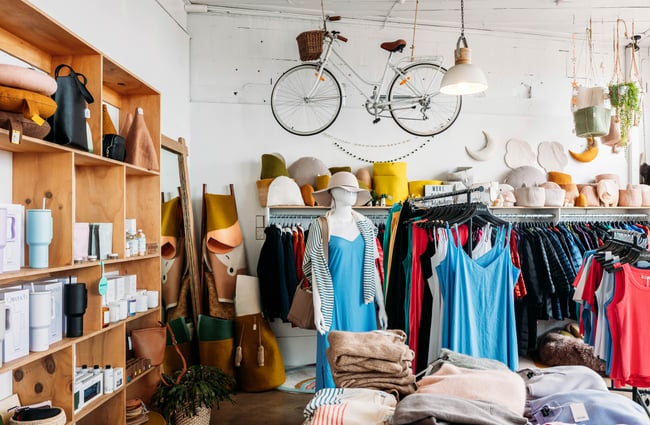 Interior of William Bee in Ōamaru with racks of women's clothing next to a shelf of accessories, felted homeware and a bicycle suspended from the ceiling