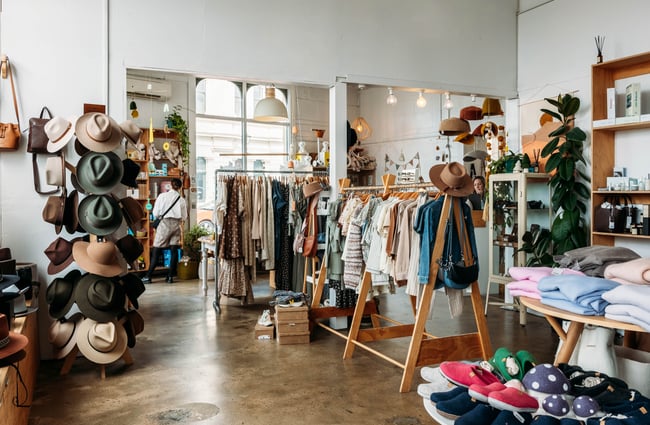 Modern shop interior filled with clothing, hats, bags and children's toys with a woman looking at a shelf of products at the front of the shop
