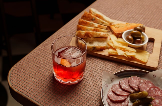 A close up of a cocktail and plates of food on a table.