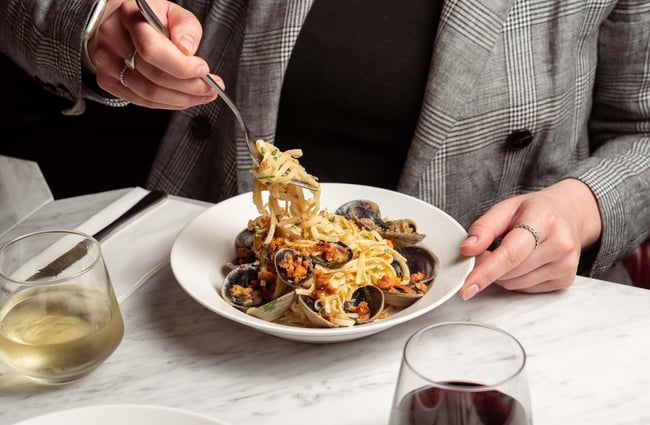 A hand holding a fork in seafood pasta.