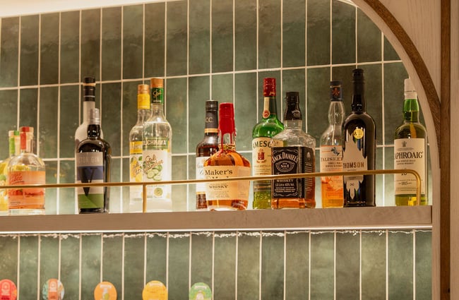 Liquor bottles lined up in a row in front of a green wall.