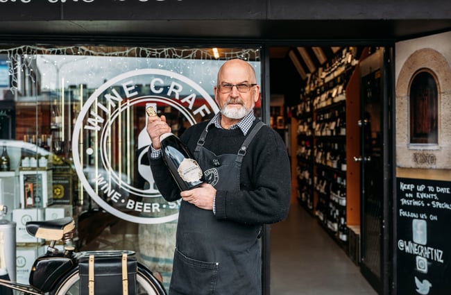 Owner holding a bottle of wine standing outside Wine Craft.