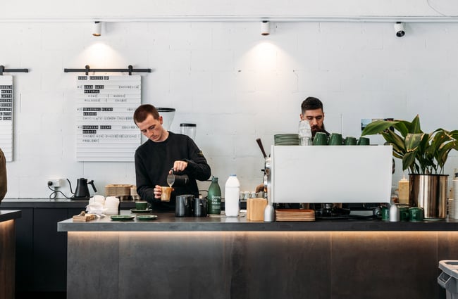 Two men working behind a cafe counter making coffee.