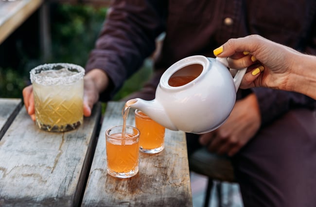 A teapot of liquor being poured into glasses.