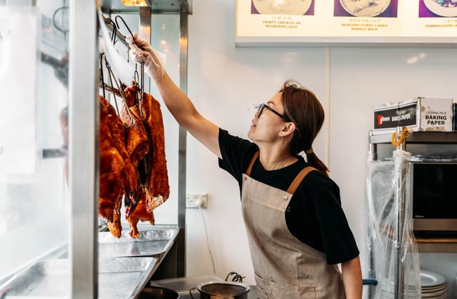 Shop assistant taking down poultry from the window at Yan's Supermarket.