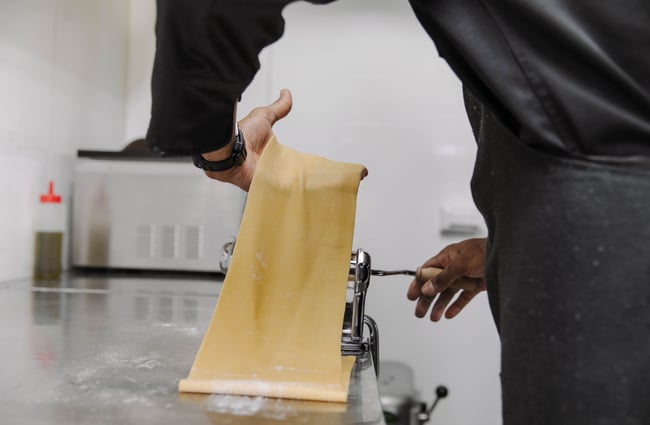 Chef hand rolling sheet of pasta inside Zephyr kitchen.