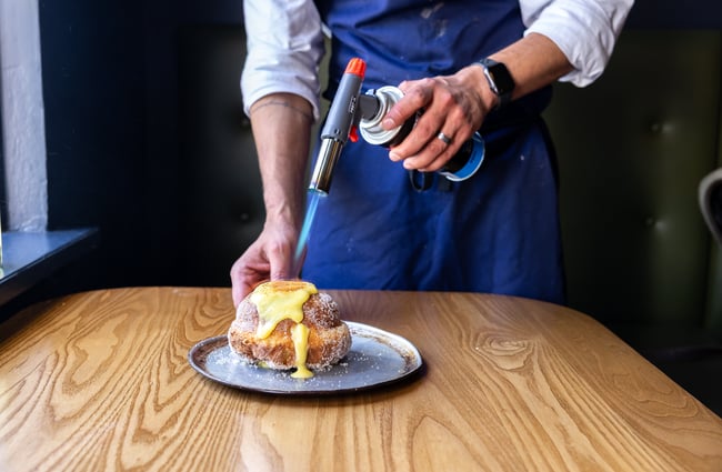 Server using a blowtorch on a creme brulee donut at Zoyi.