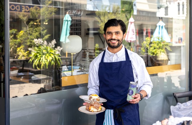 Owner holding plates of cinnamon rolls and drink in a can at Zoyi.