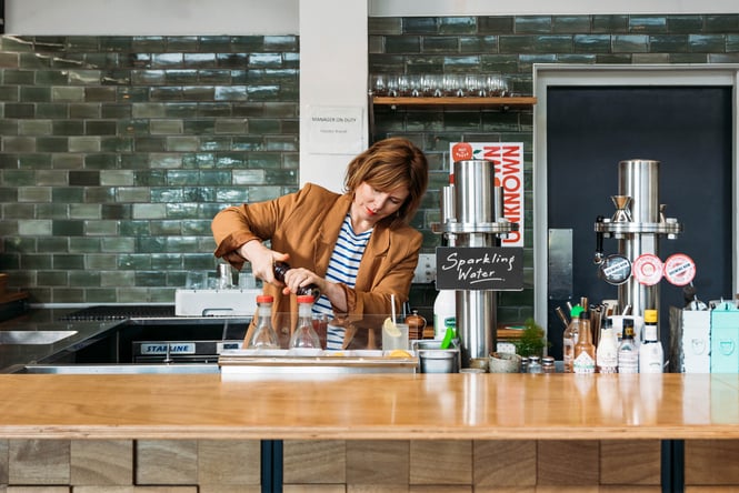 A woman making a cocktail behind a bar.