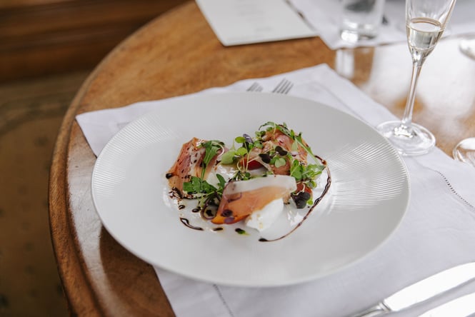 Fancily presented plate of cured meats and microherbs on a table with a white linen placemat.