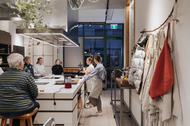 People standing around a test kitchen as two women present.