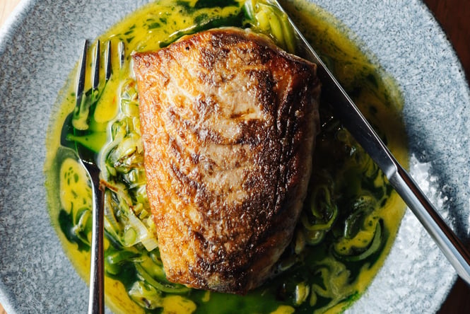 Close up of a seared fillet of fish in a shallow bowl of sauce at 5th Street restaurant Christchurch.