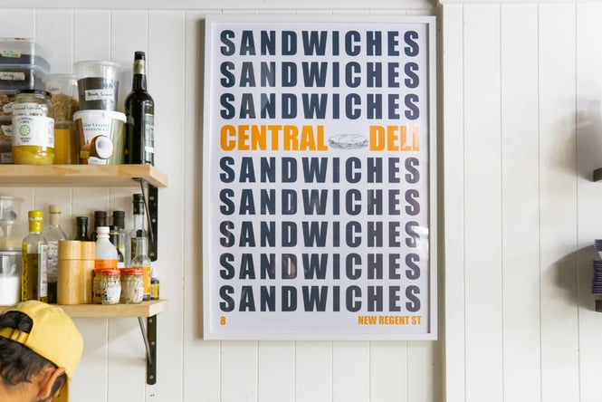 A large Central Deli Sandwiches poster framed on a wall.