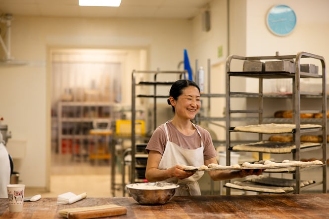 A female chef moves a tray of proving dough rolls.