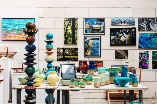 Unique sculptures and ceramics on table in front of a wall filled with artistic photography at Crafted Gallery in Ōamaru