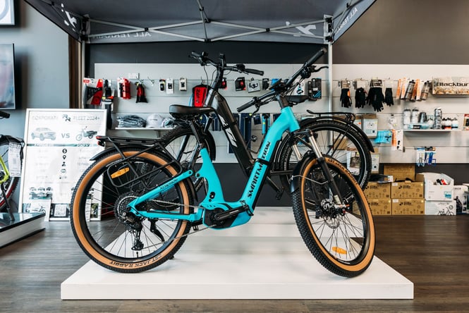 An electric blue e-bike displayed on a low white plinth inside Electrify.