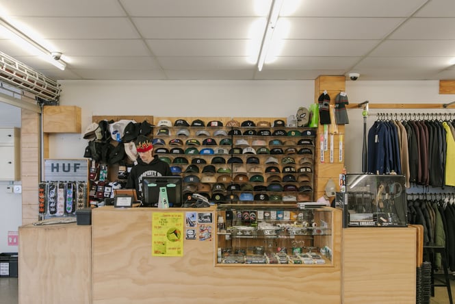 A man working behind the counter at Embassy where lots of caps are displayed on shelves.
