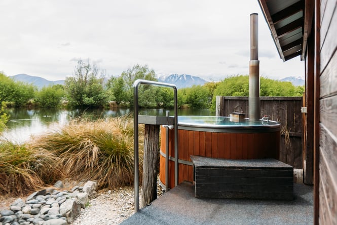 Cedar hot tub next to a small lake looking out towards snowy mountain peaks